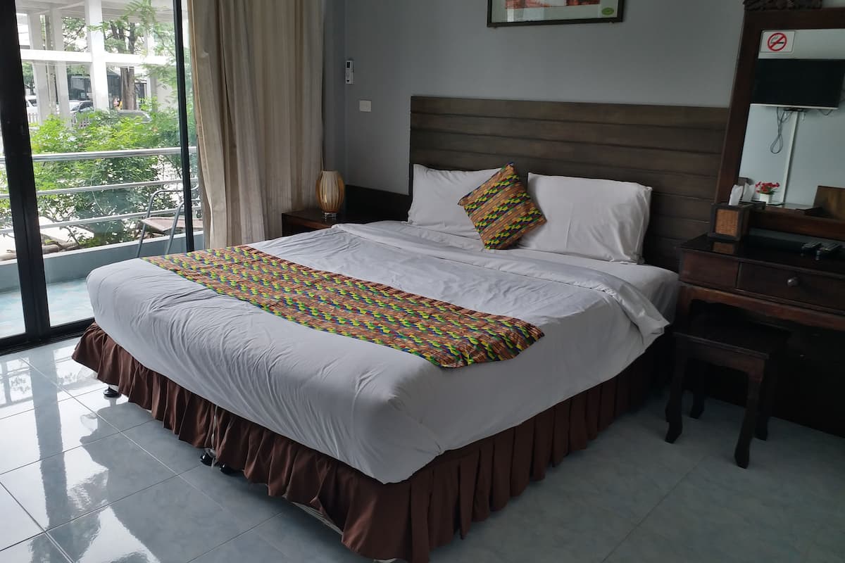 A hotel room with a large bed, a nightstand, a bedside table, a window with curtains, and a view of a building outside.