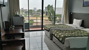 Une chambre d’hôtel avec deux lits, un bureau et un balcon donnant sur la ville.