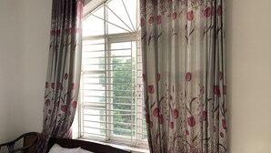 Un dormitorio con dos camas, una ventana con persianas y cortinas estampadas con motivos florales.