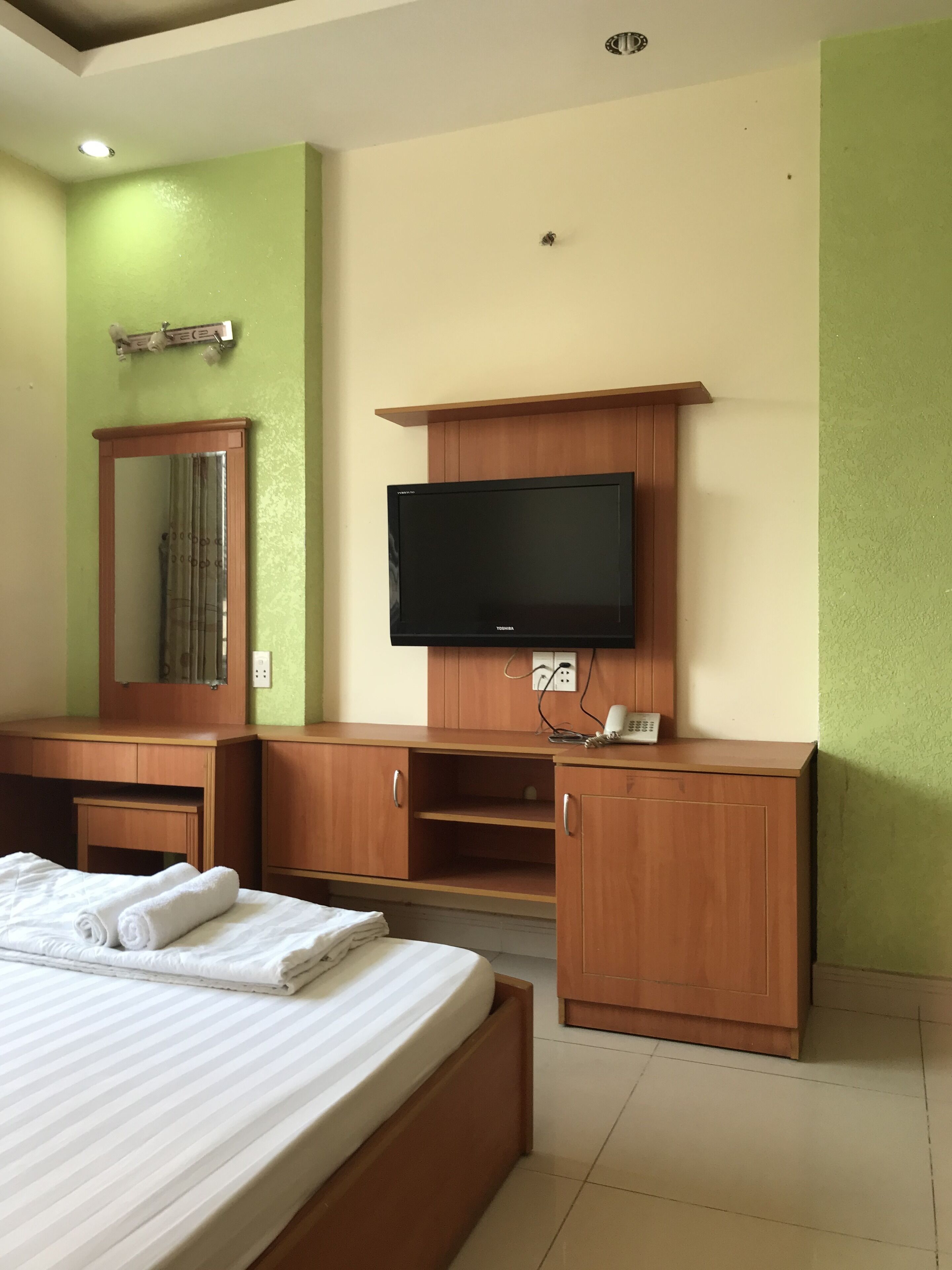A hotel room with a bed, wooden furniture, a flat-screen TV, and a mirror.
