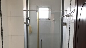 Une salle de bain comprenant des toilettes, une douche fermée par une paroi de verre et une porte dotée d’une poignée.