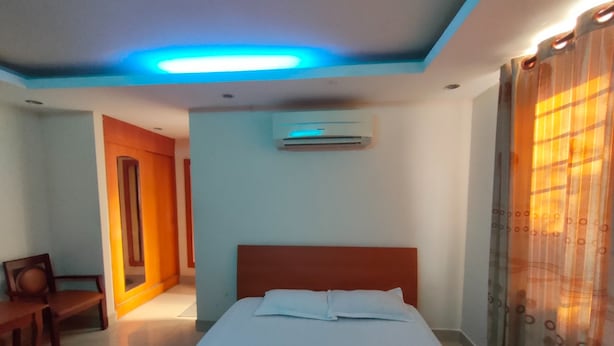 Une chambre d’hôtel comprenant un lit, un appareil de climatisation, une chaise en bois et une porte donnant sur une autre pièce.