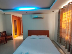 Ein Hotelzimmer mit einem Bett, einer Klimaanlage, einem Holzstuhl und einer Tür zu einem anderen Raum.