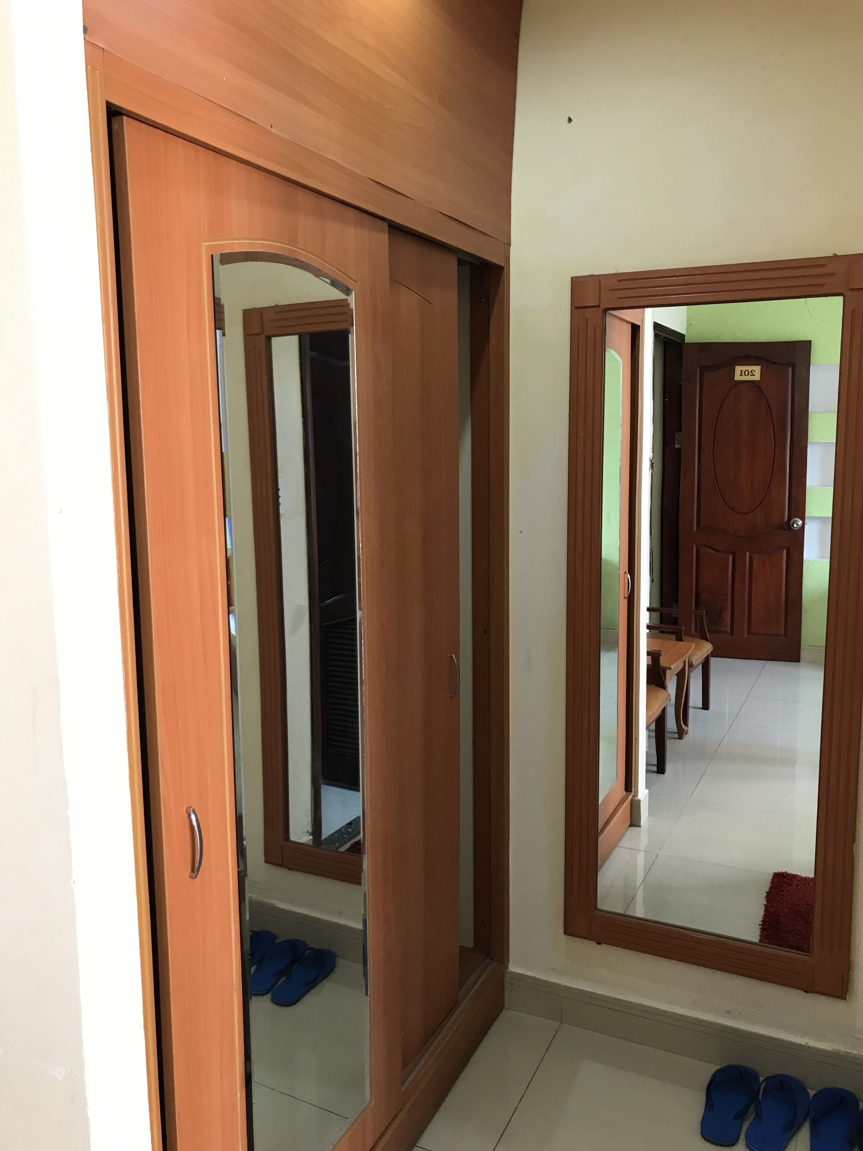 A room with a wooden wardrobe, a mirror, and a door with a number plate.