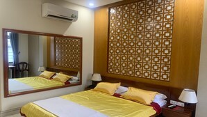 A hotel room with a large bed, a wooden headboard, a decorative panel, a nightstand with a lamp, and a mirror. - Phu Si Hotel (Ho Chi Minh City)