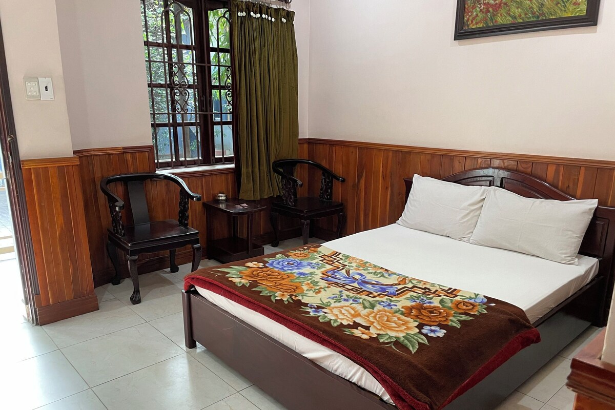 A bedroom with a bed, two chairs, a small table, and a window with curtains.