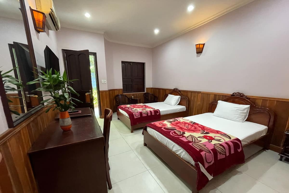 A hotel room with two single beds, a wooden desk, a chair, a potted plant, and a mirror.