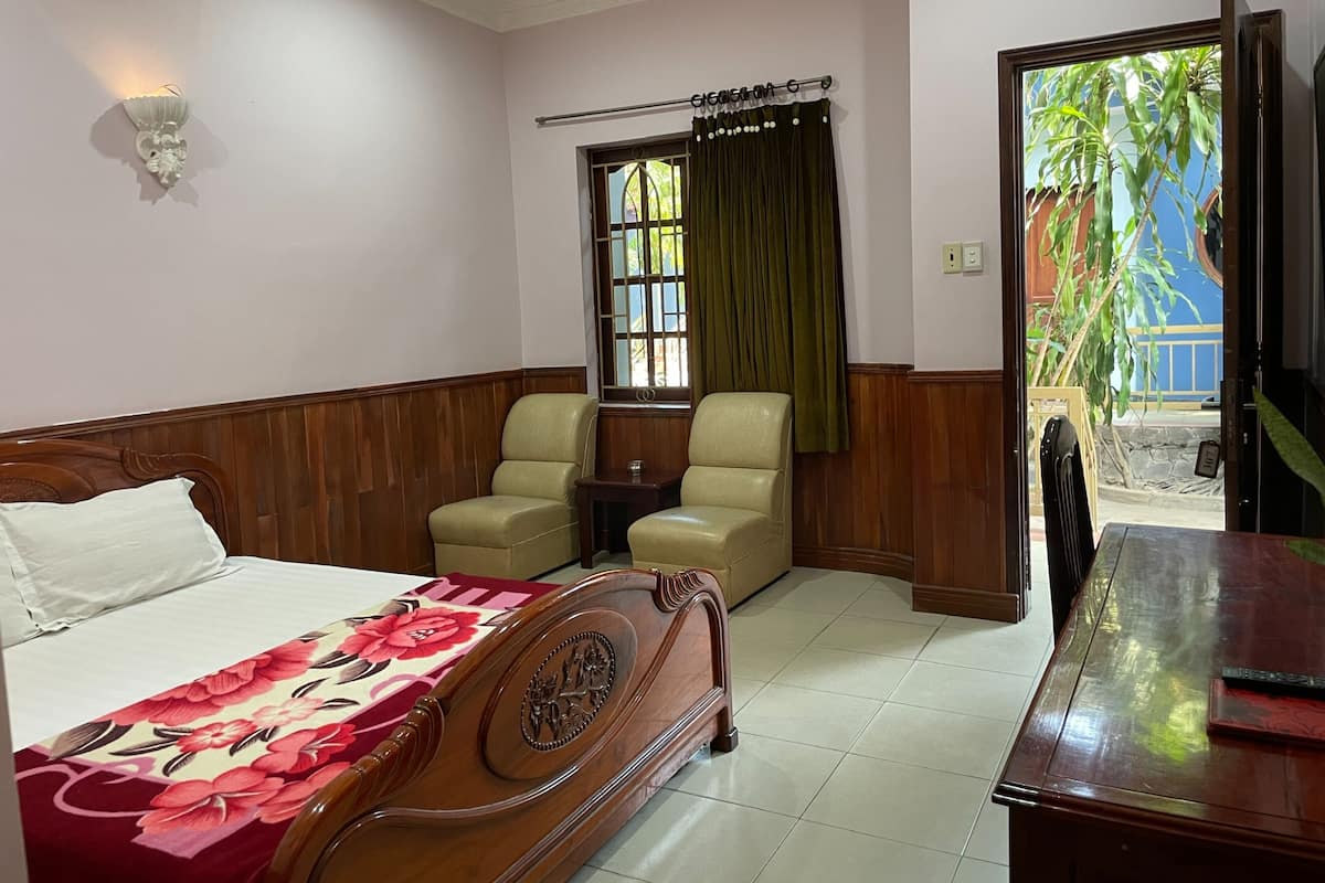 A hotel room with a bed, two chairs, a small table, a window with curtains, and a view of the outside.