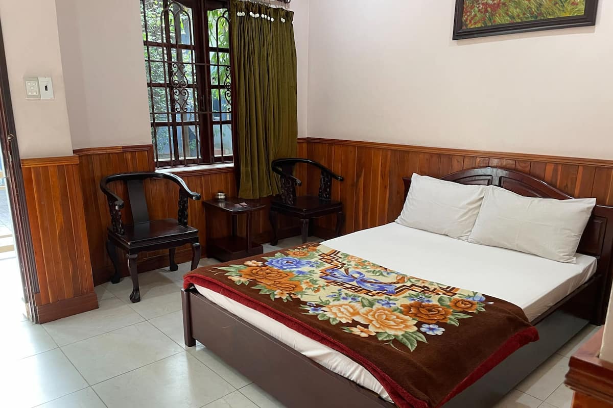 A bedroom with a bed, two chairs, a small table, and a window with curtains.