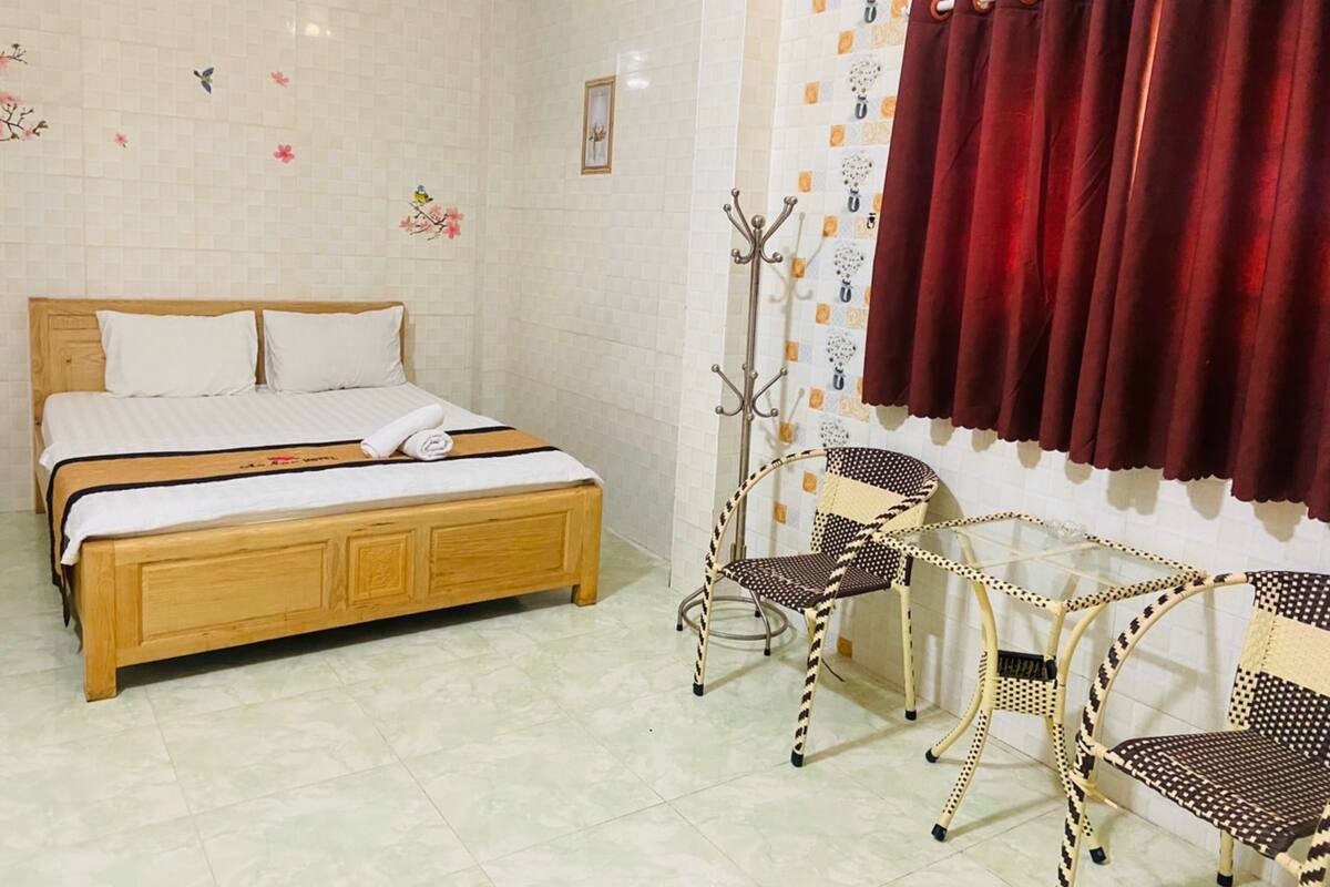 A hotel room with a wooden bed, a small table with chairs, and a red curtain.
