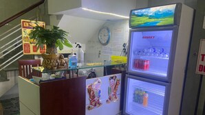 Un espace d’accueil avec un réfrigérateur rempli de boissons, une horloge au mur et une plante sur le comptoir.