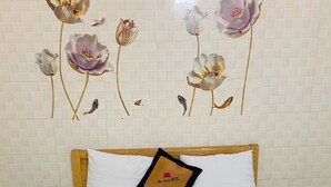 Une chambre d’hôtel avec un lit, un oreiller orné du logo de l’hôtel, une serviette et un mur décoré d’œuvres d’art florales.