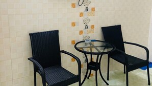 Une petite pièce avec un téléviseur fixé au mur, deux chaises noires et une table en verre.