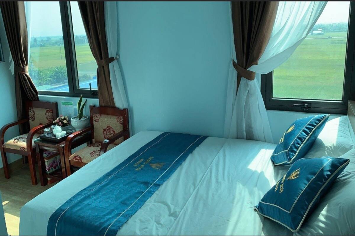 Une chambre avec un lit, un bureau, des chaises et une vue sur un champ verdoyant par la fenêtre.