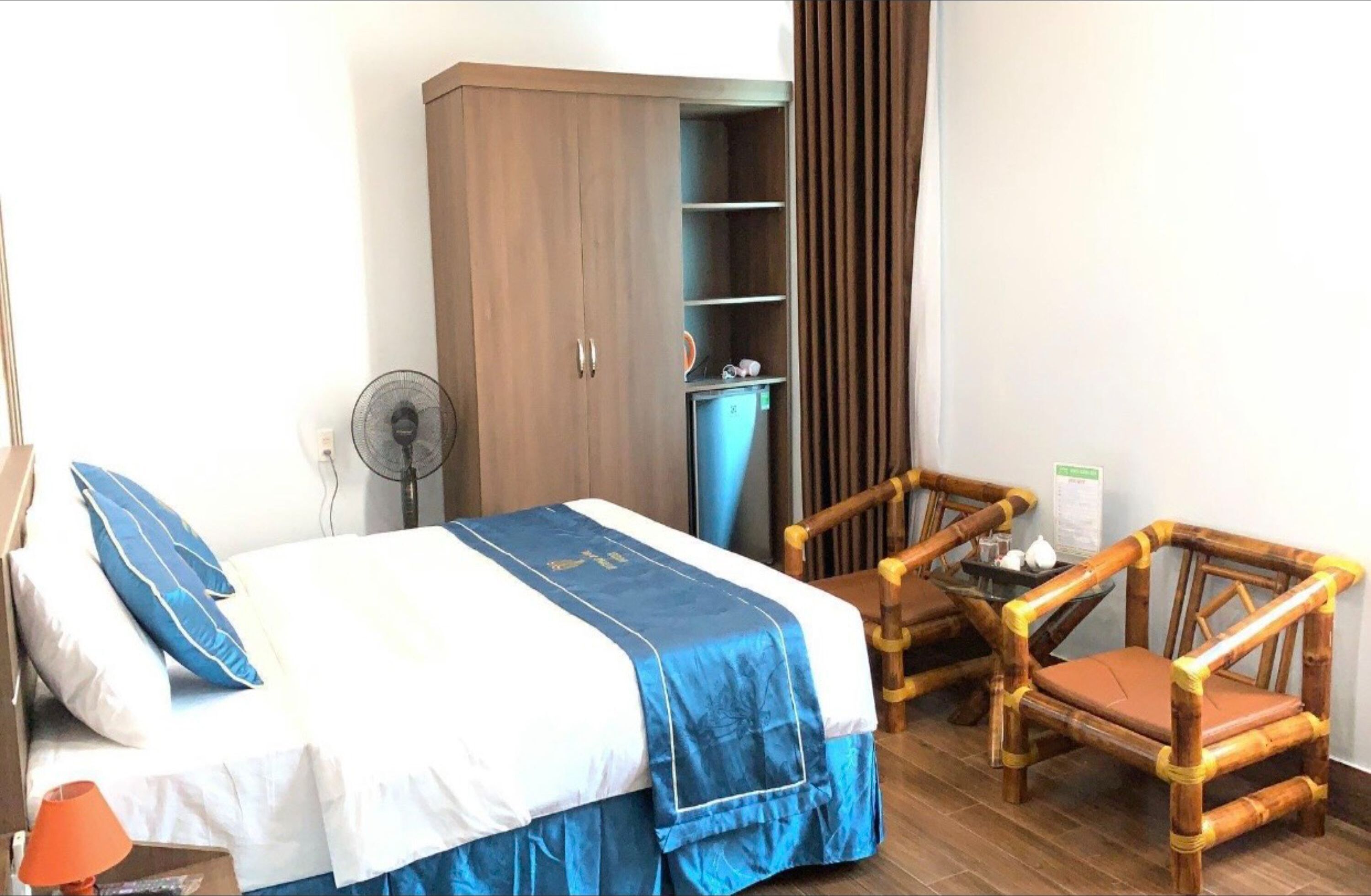 A bedroom with a bed, a wardrobe, a fan, a chair, and a small table with items on it.