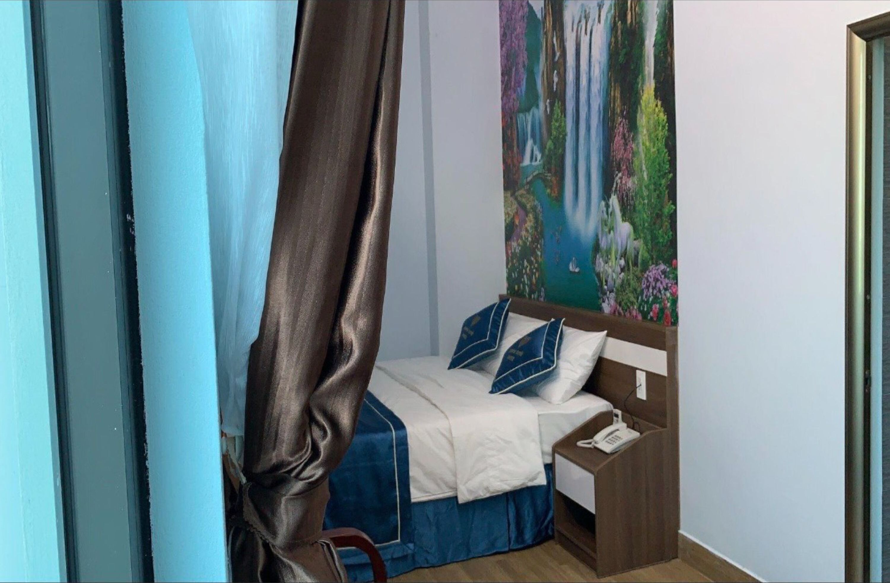 Une chambre à coucher avec un lit, une table de chevet, un tableau au mur et un rideau.