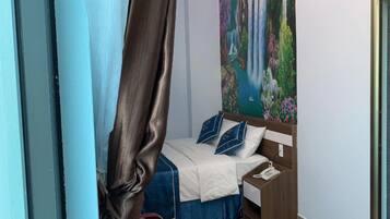 Une chambre à coucher avec un lit, une table de chevet, un tableau au mur et un rideau.