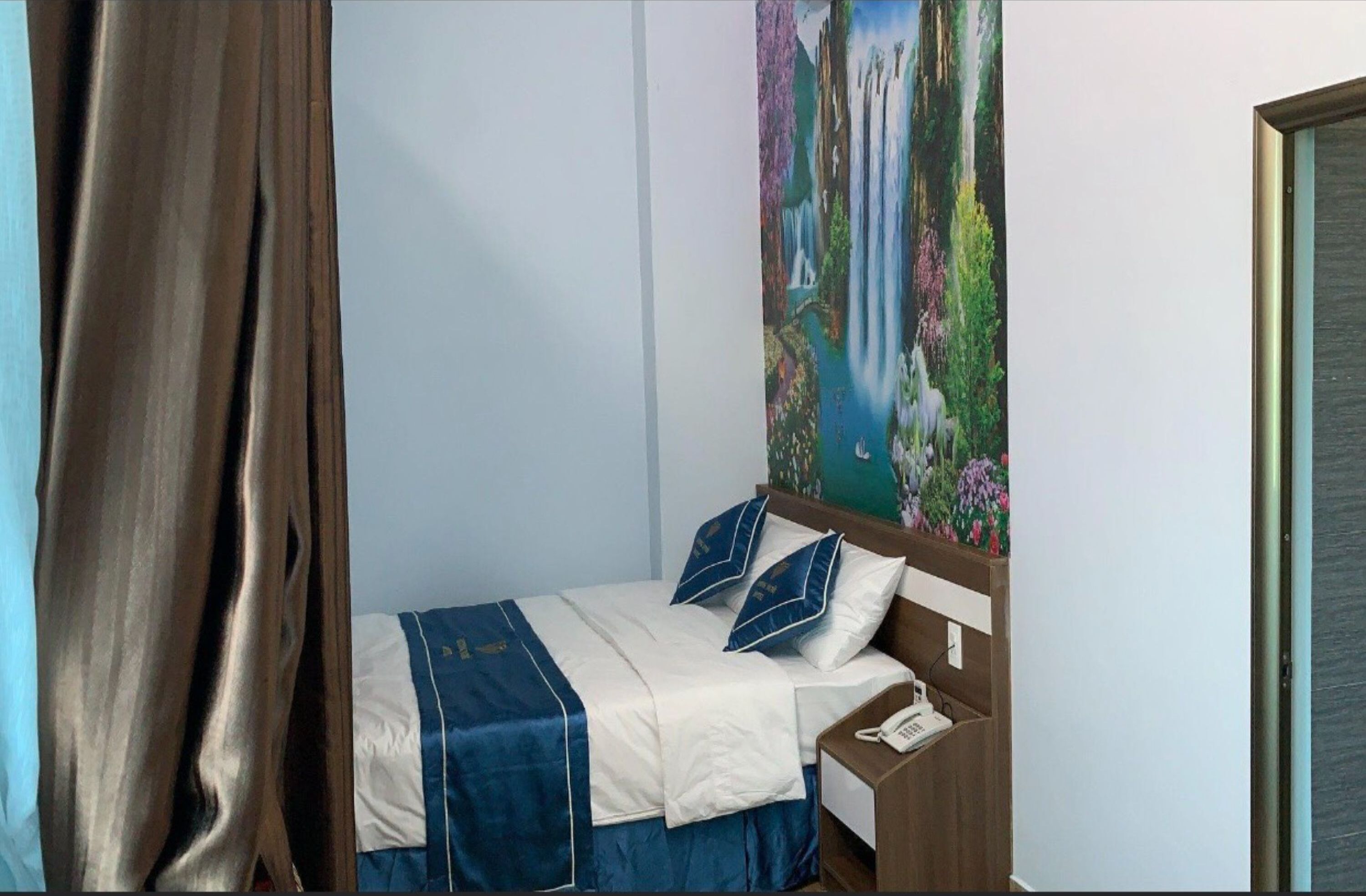 A hotel room with a bed, a nightstand, a telephone, and a painting of a waterfall on the wall.