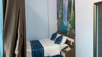 A hotel room with a bed, a nightstand, a telephone, and a painting of a waterfall on the wall.