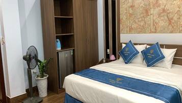 Une chambre d’hôtel avec un lit, une armoire, un ventilateur, une plante en pot et un mur décoratif.
