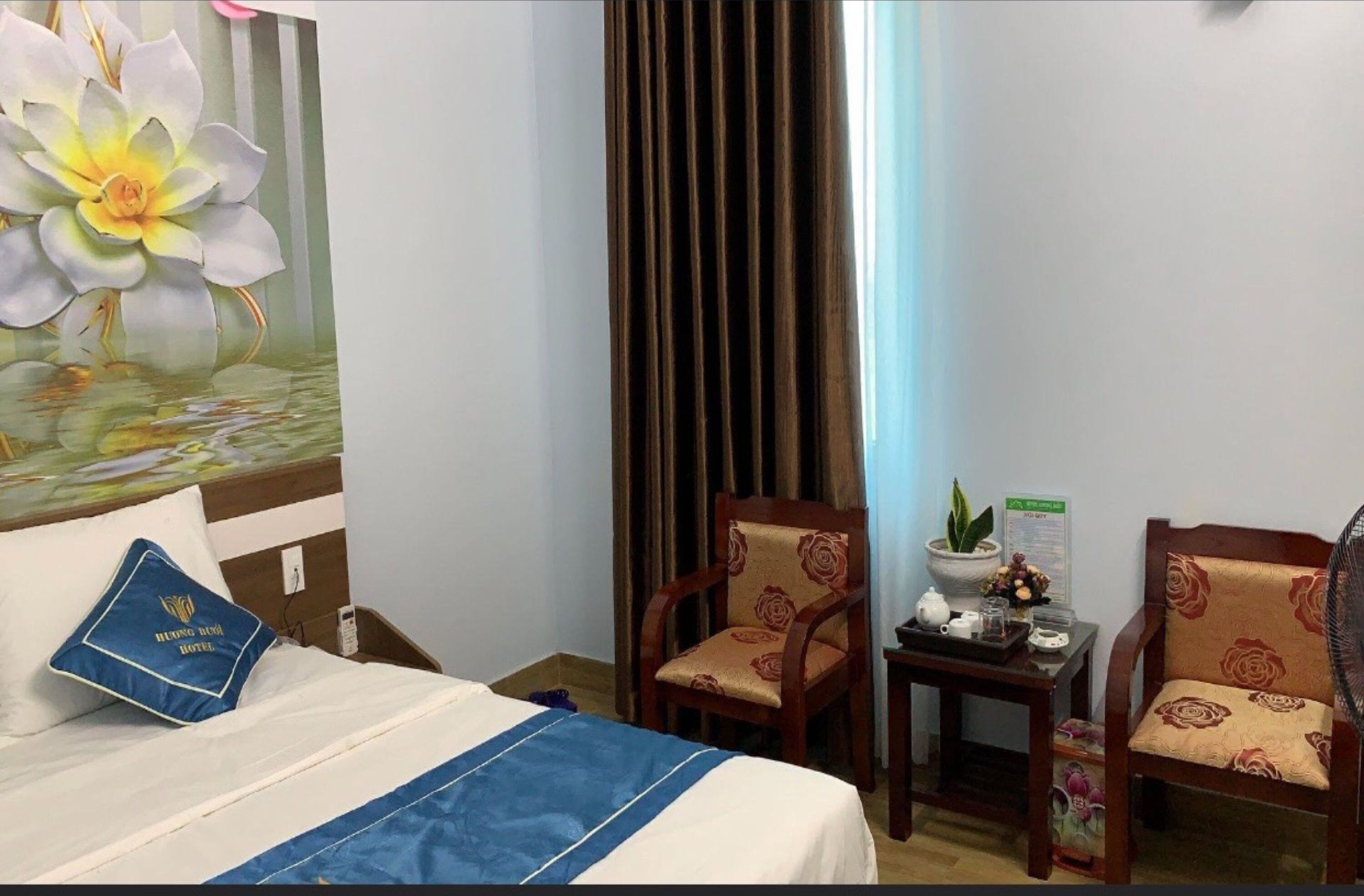 Een hotelkamer met een bed, twee stoelen, een kleine tafel met een plant, en een schilderij van een bloem.