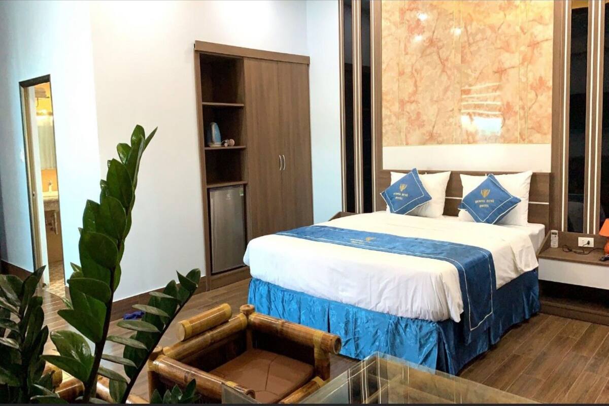 Une chambre d’hôtel avec un grand lit, une armoire, un miroir et une plante.