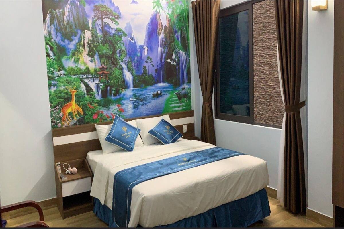 Une chambre à coucher comprenant un lit, une table de chevet, une fenêtre avec des rideaux et une fresque murale.