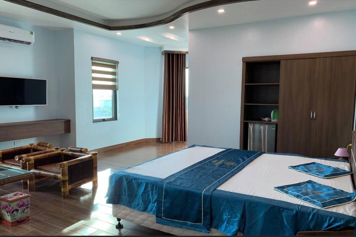 Une chambre d’hôtel avec un grand lit, un téléviseur fixé au mur, une armoire en bois, un bureau avec une lampe et une fenêtre avec des rideaux.