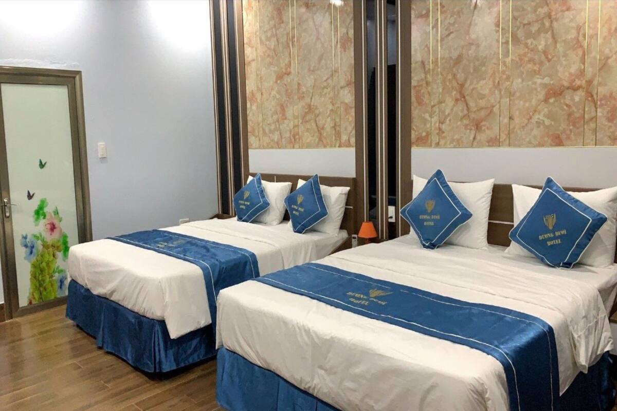 Une chambre d’hôtel avec deux lits, chacun recouvert d’une couverture bleue assortie aux oreillers, et un grand miroir au-dessus des lits.