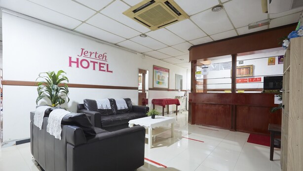 A hotel reception area with a reception desk, a black sofa, a small table with a plant, and a wall with the hotel's name. - Jerteh Hotel, Terengganu (Jerteh)