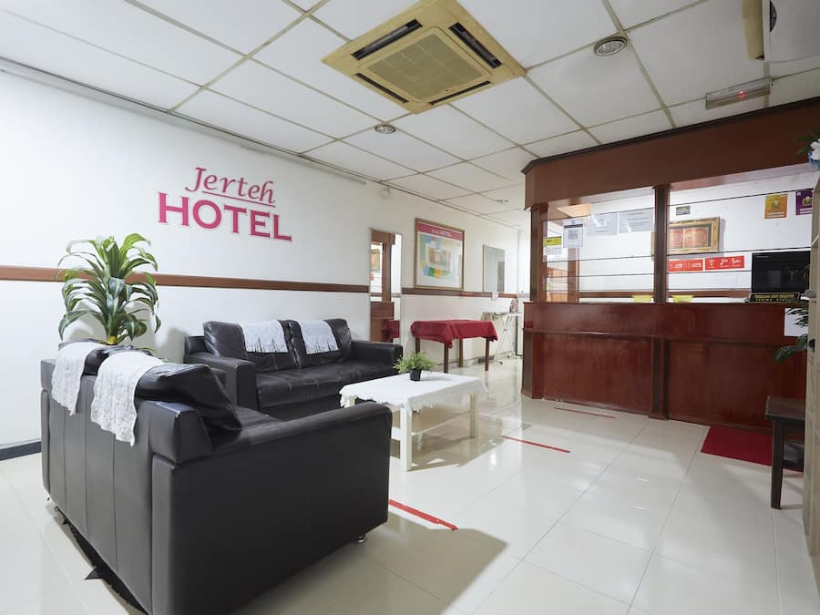 A hotel reception area with a reception desk, a black sofa, a small table with a plant, and a wall with the hotel's name.