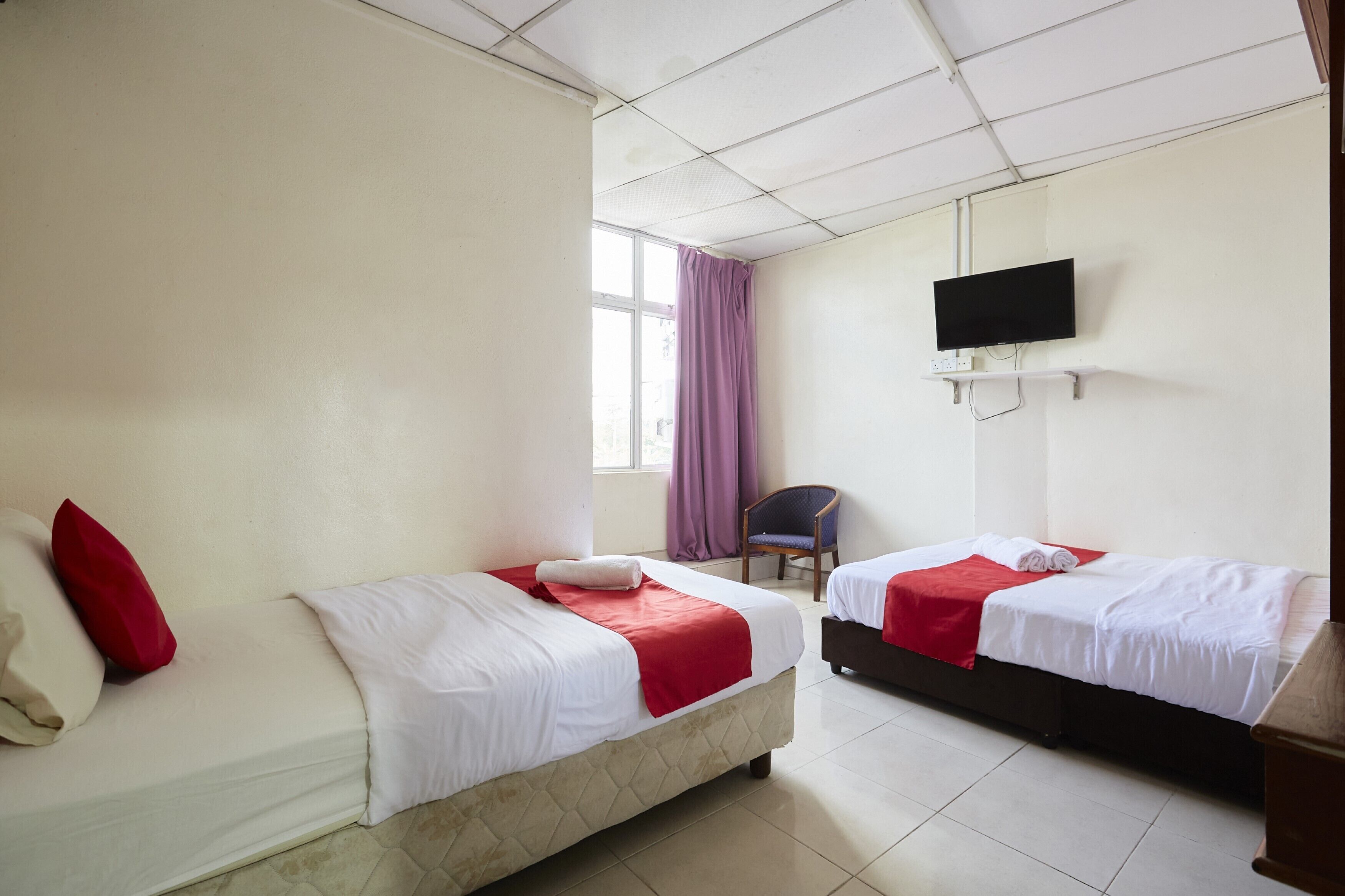Habitación de hotel con dos camas, un televisor montado en la pared y una ventana con cortinas.