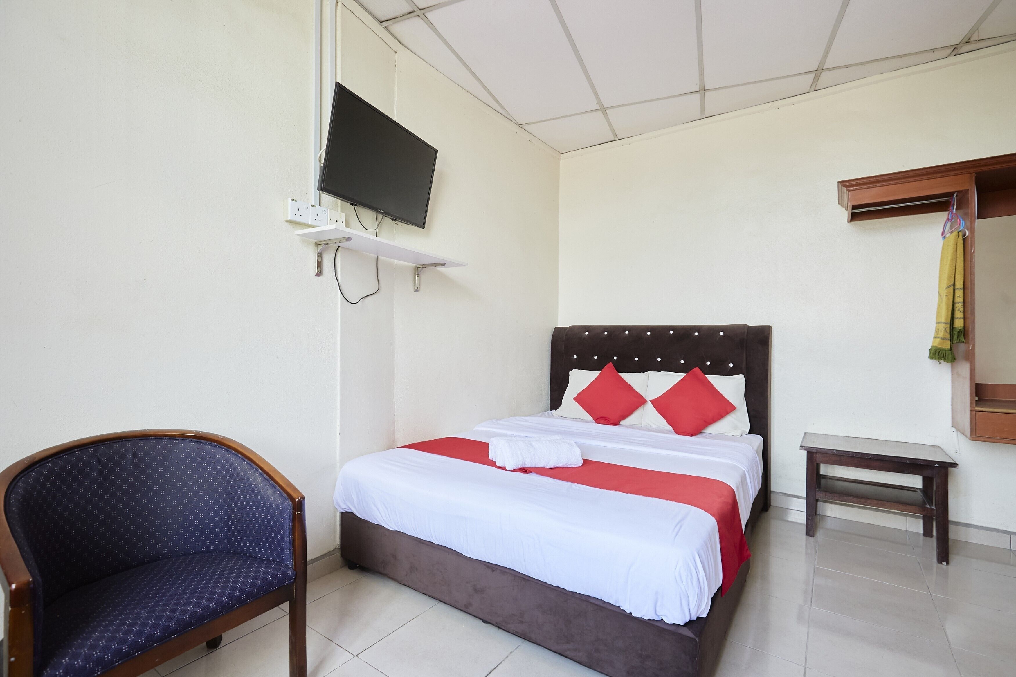 Camera d'albergo con un letto, una sedia, un tavolino, una TV a parete e uno specchio.
