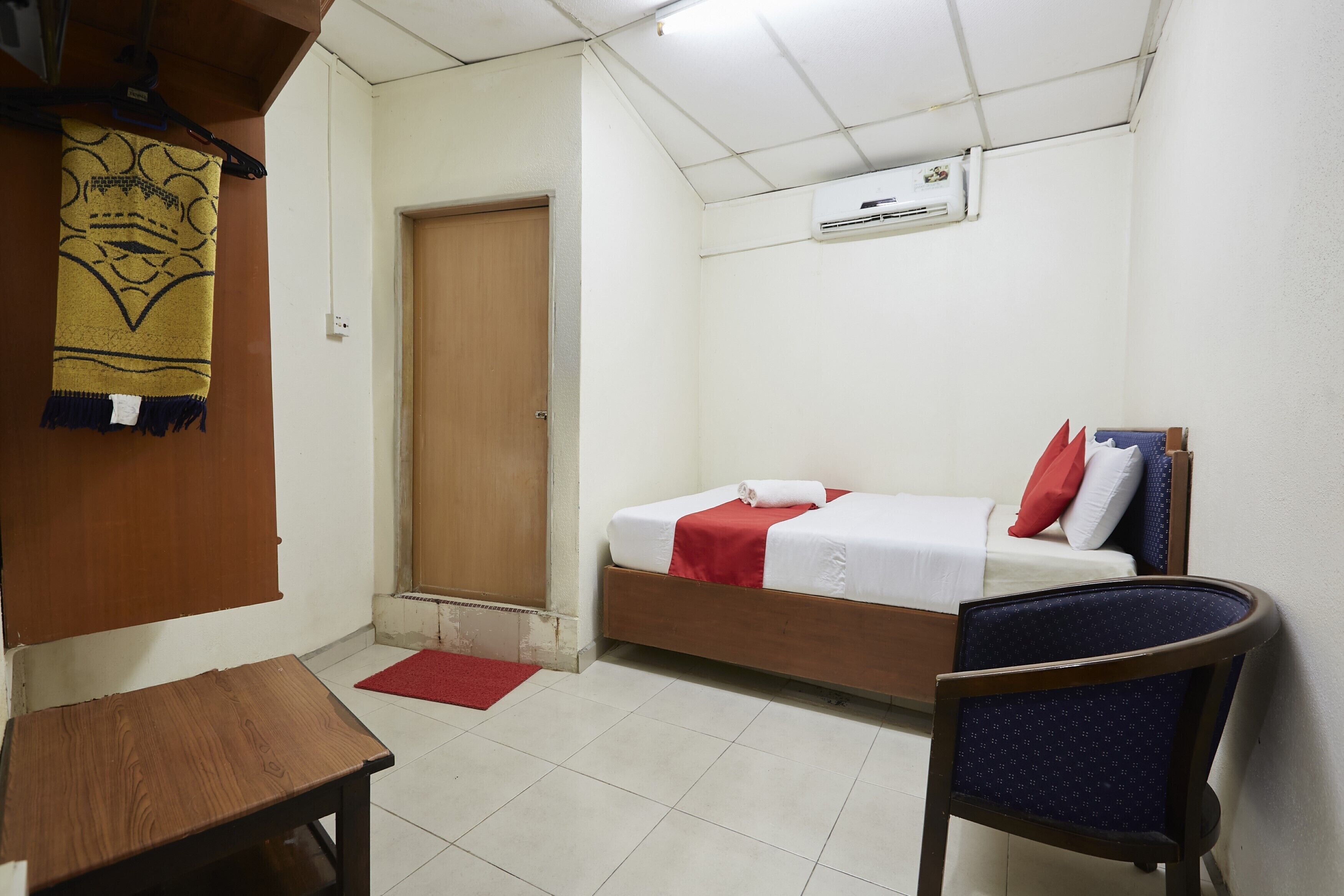 Una habitación pequeña y limpia con una cama individual, una mesa de madera, una silla y un tapete rojo en el suelo.