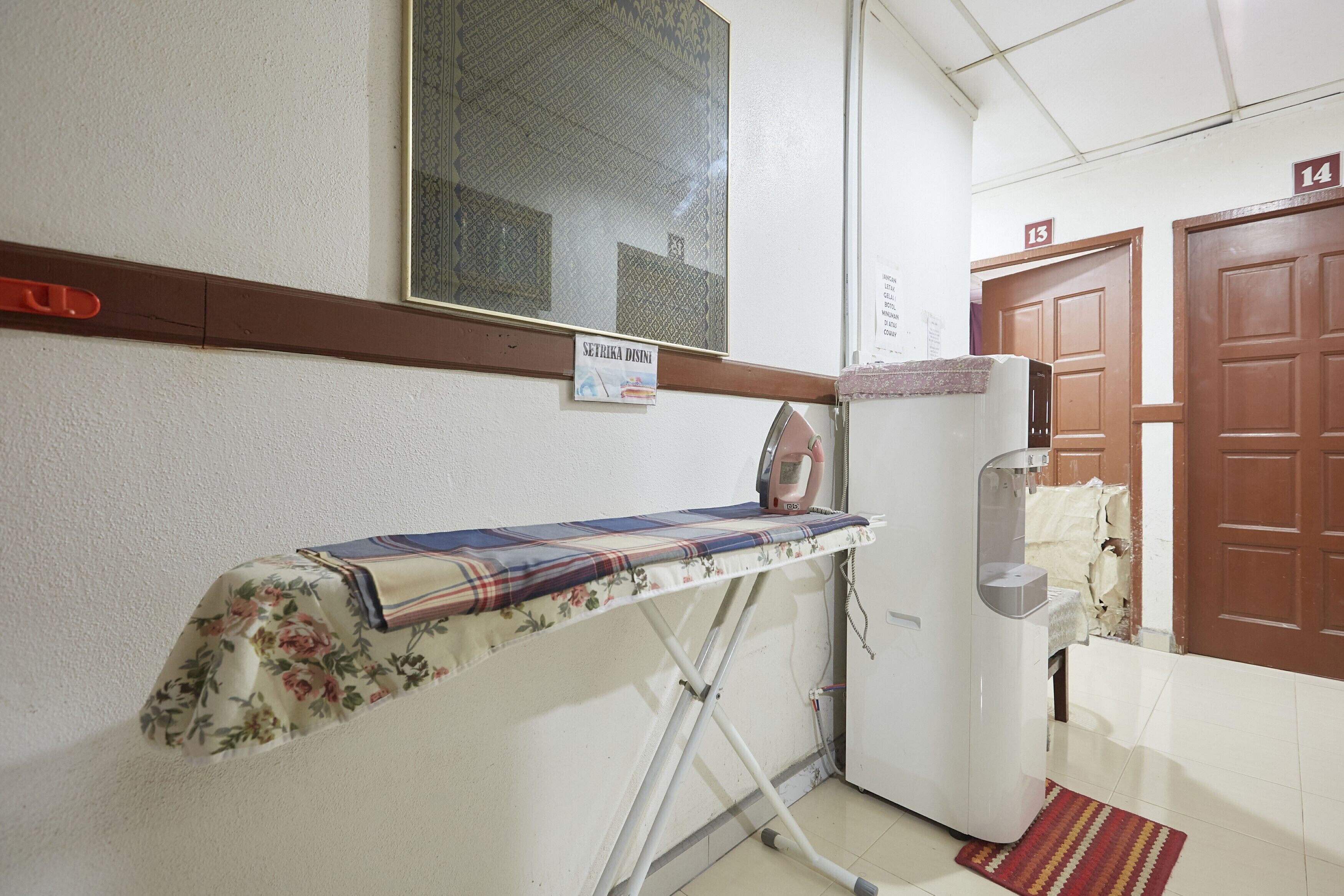 A room with a wall-mounted ironing board, a water heater, and a door with the number 14.