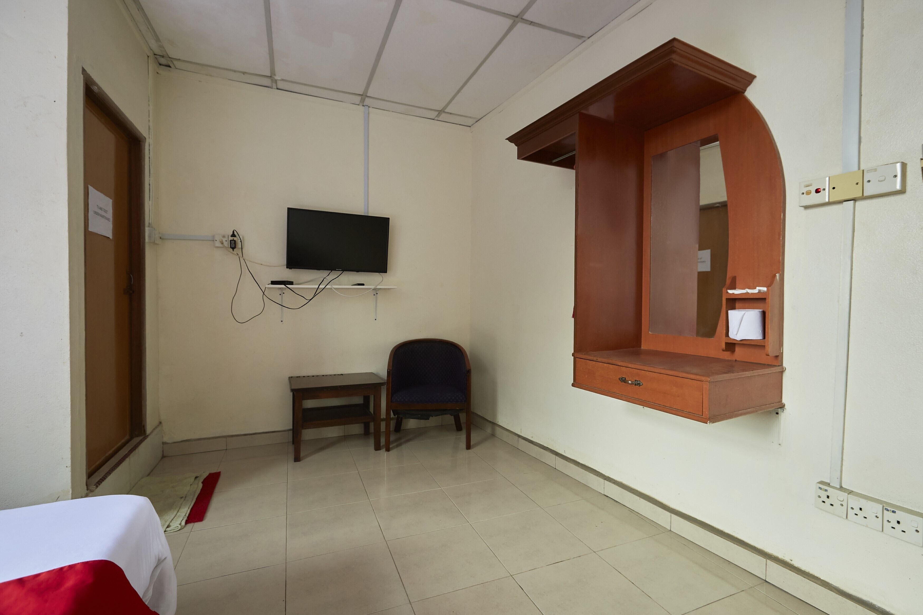 A hotel room with a bed, a desk, a chair, a television mounted on the wall, and a wooden cabinet with a mirror.