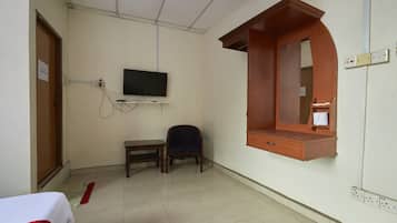 A hotel room with a bed, a desk, a chair, a television mounted on the wall, and a wooden cabinet with a mirror.