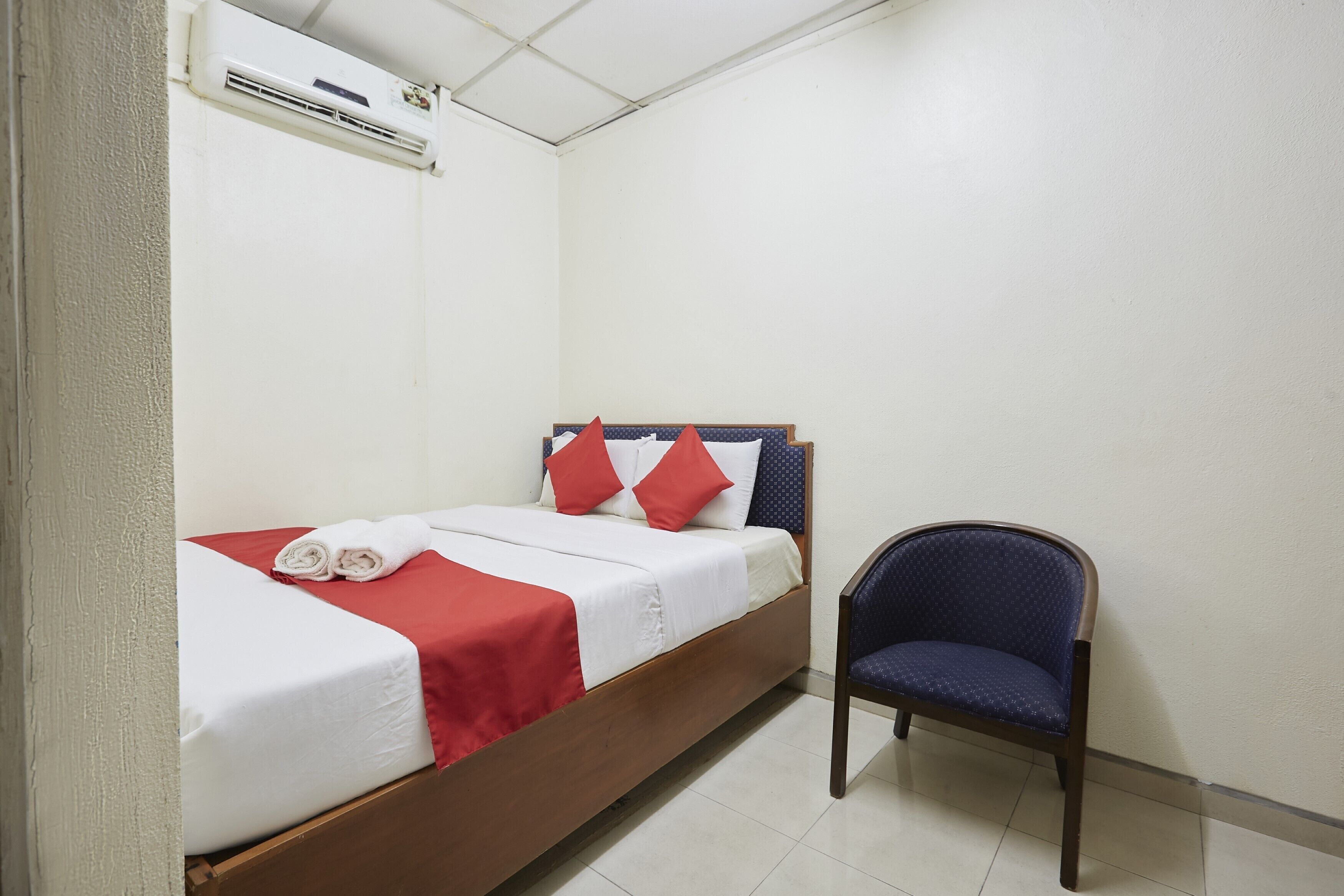 A single bed with red and white bedding, a blue chair, and an air conditioning unit on the wall.