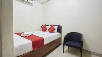 A single bed with red and white bedding, a blue chair, and an air conditioning unit on the wall.