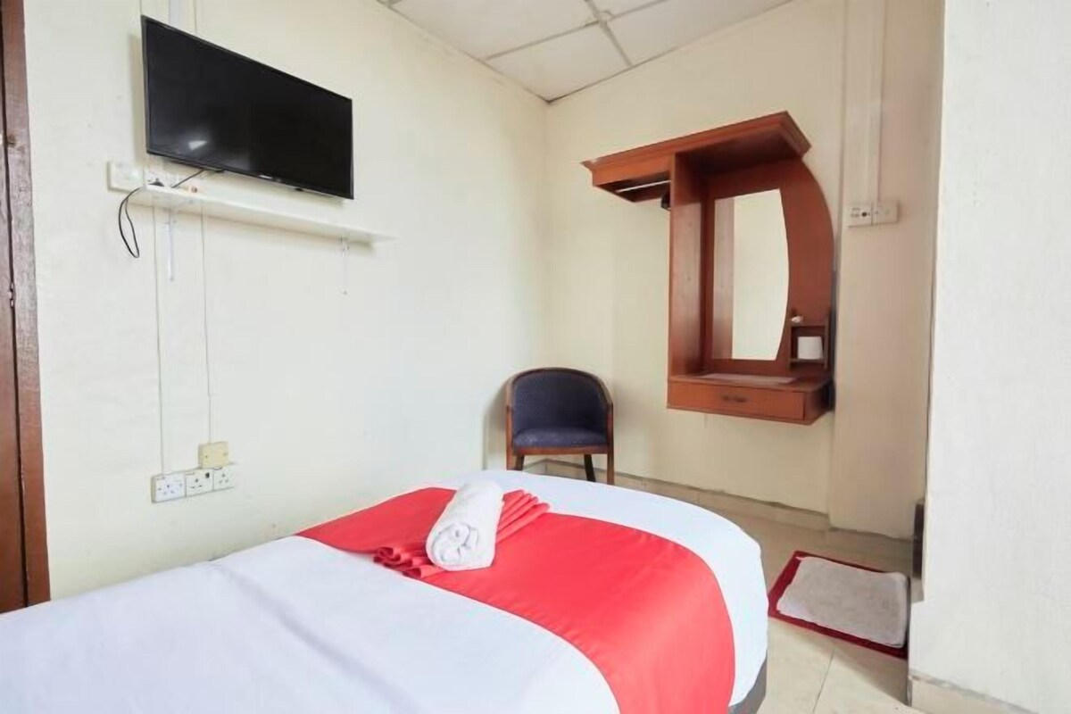 A hotel room with a bed, a TV mounted on the wall, a chair, and a wooden shelf.