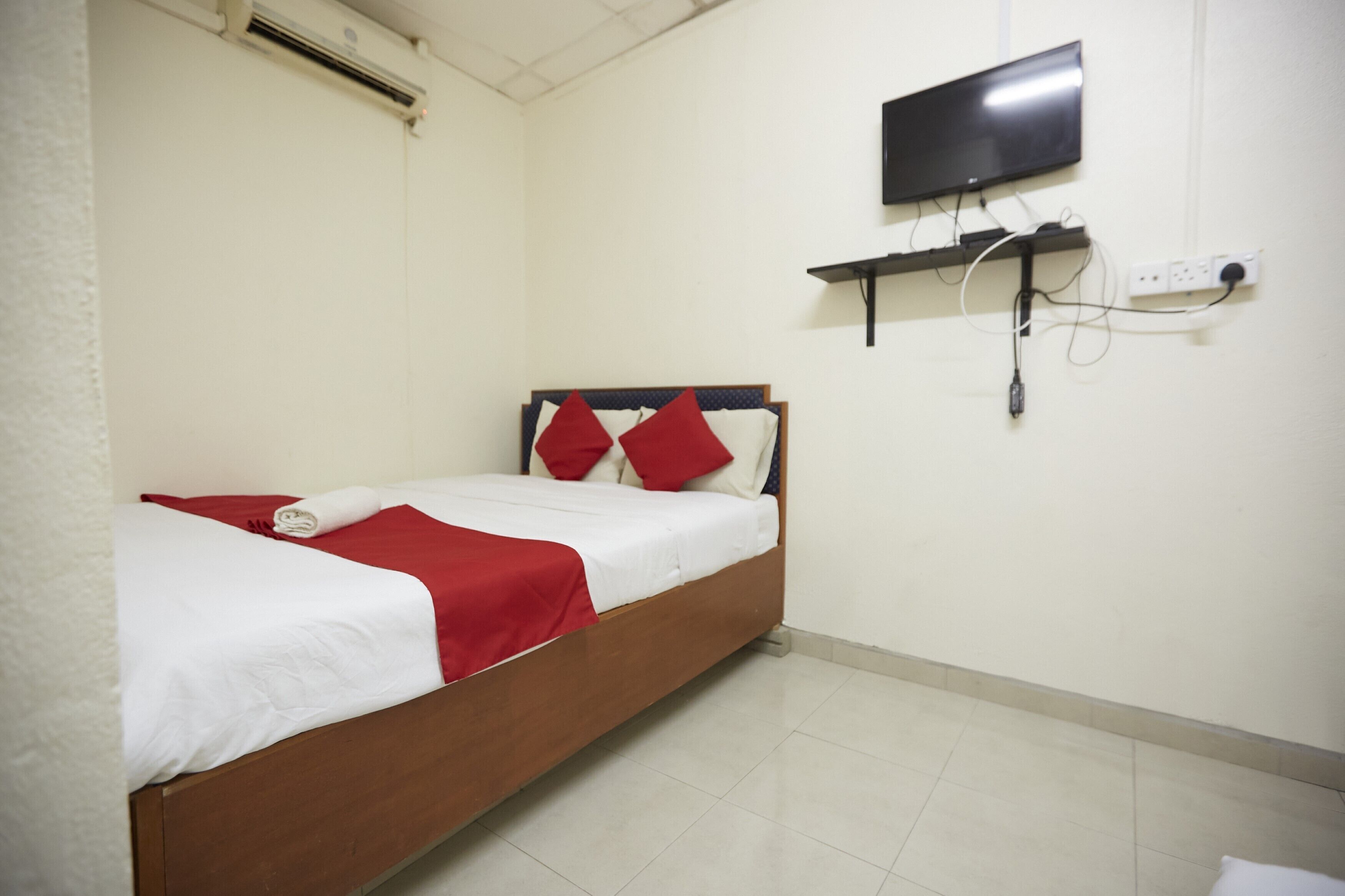 A neatly made bed with red and white bedding, a mounted TV, and a power outlet on the wall.
