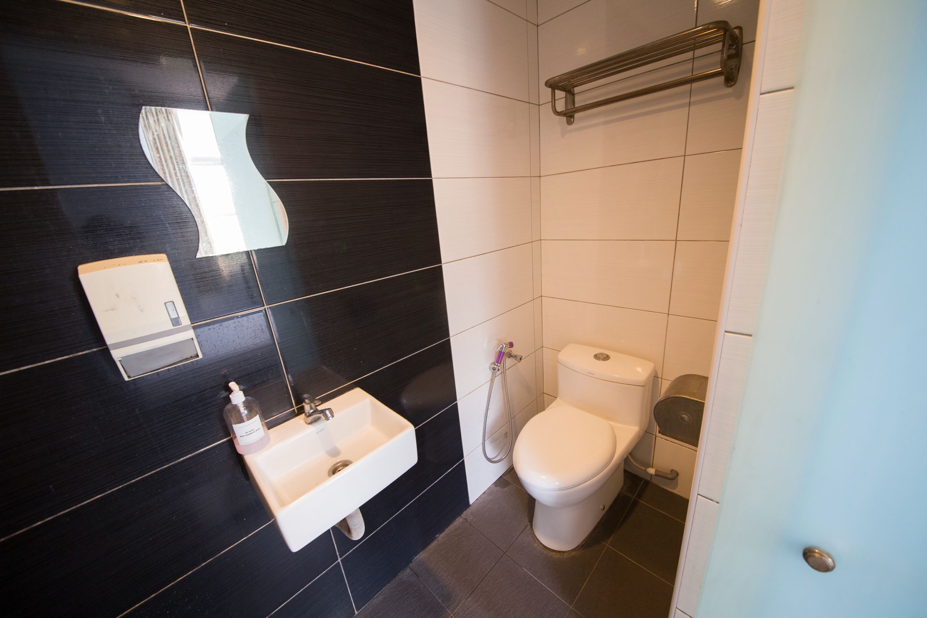 Ein modernes Badezimmer mit Wandbelag aus Schwarz-Weiß-Fliesen, einem weißen Waschbecken mit Seifenspender und einer Toilette mit einem Metall-Handtuchhalter darüber.