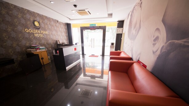 A hotel reception area with a reception desk, a red seating area, and a wall with a floral pattern and a large poster. - Golden Pearl Hotel Near Universiti Tun Hussein Onn Malaysia UTHM (Batu Pahat)