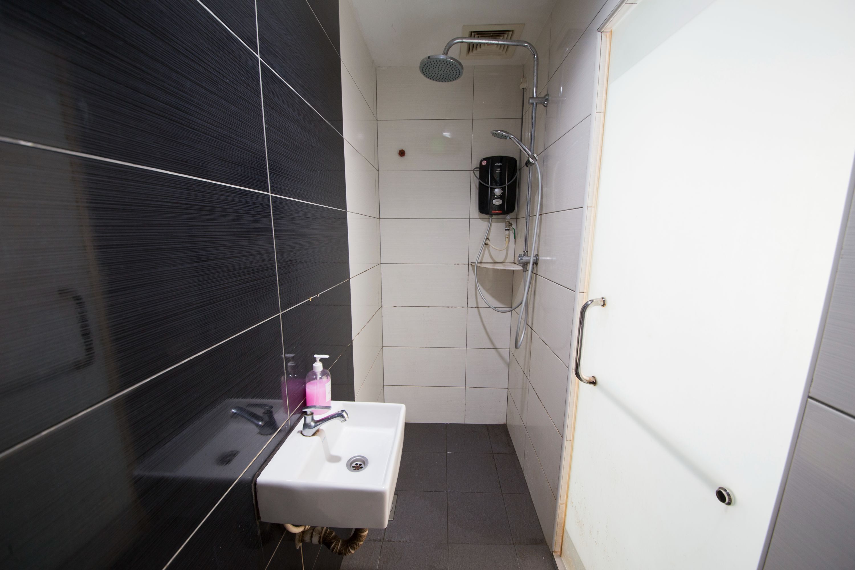A small bathroom with a white sink, a handheld showerhead, and a soap dispenser.