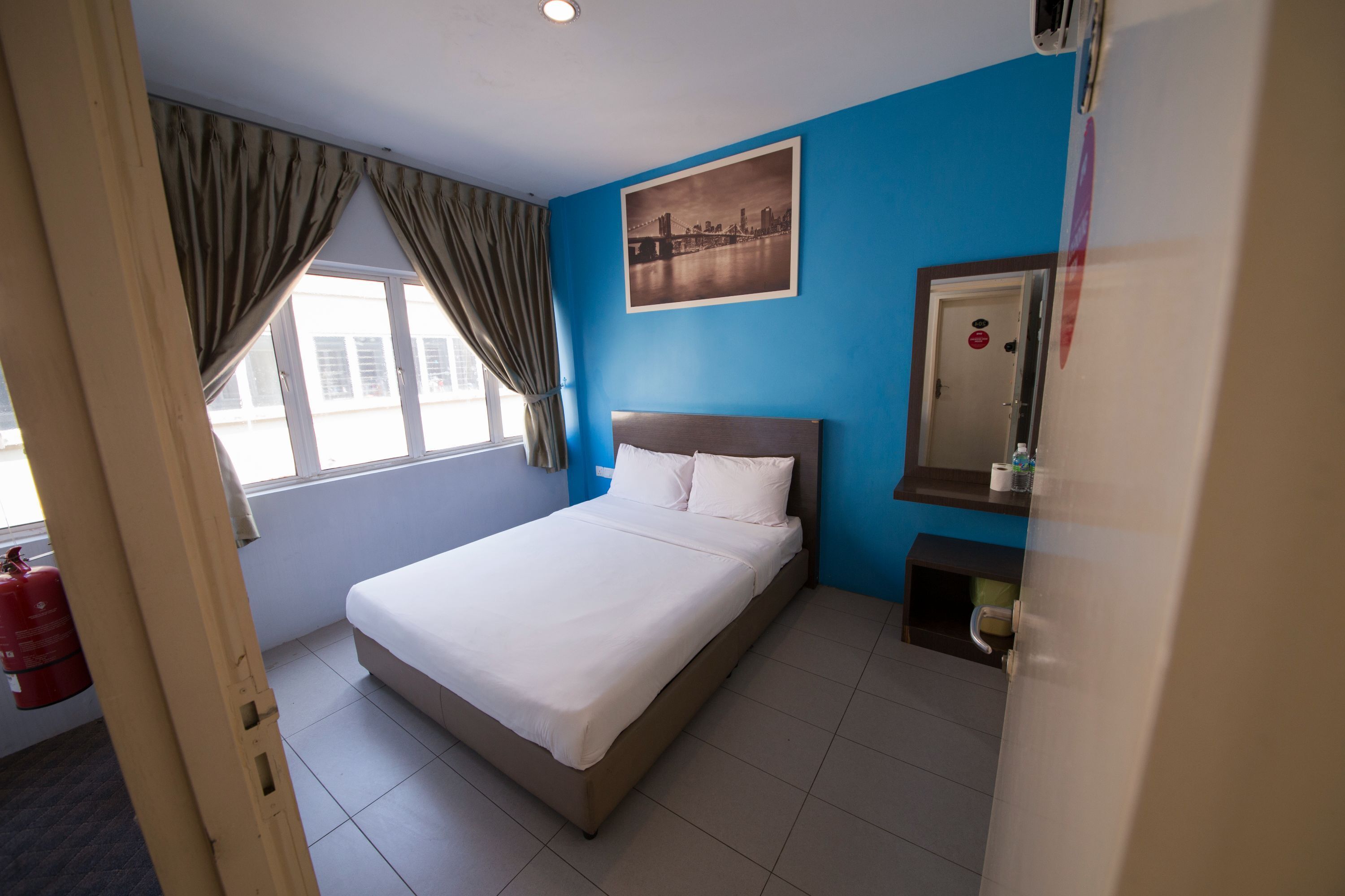 Habitación de hotel con cama, ventana con cortinas, un cuadro en la pared y una mesita de noche con espejo.
