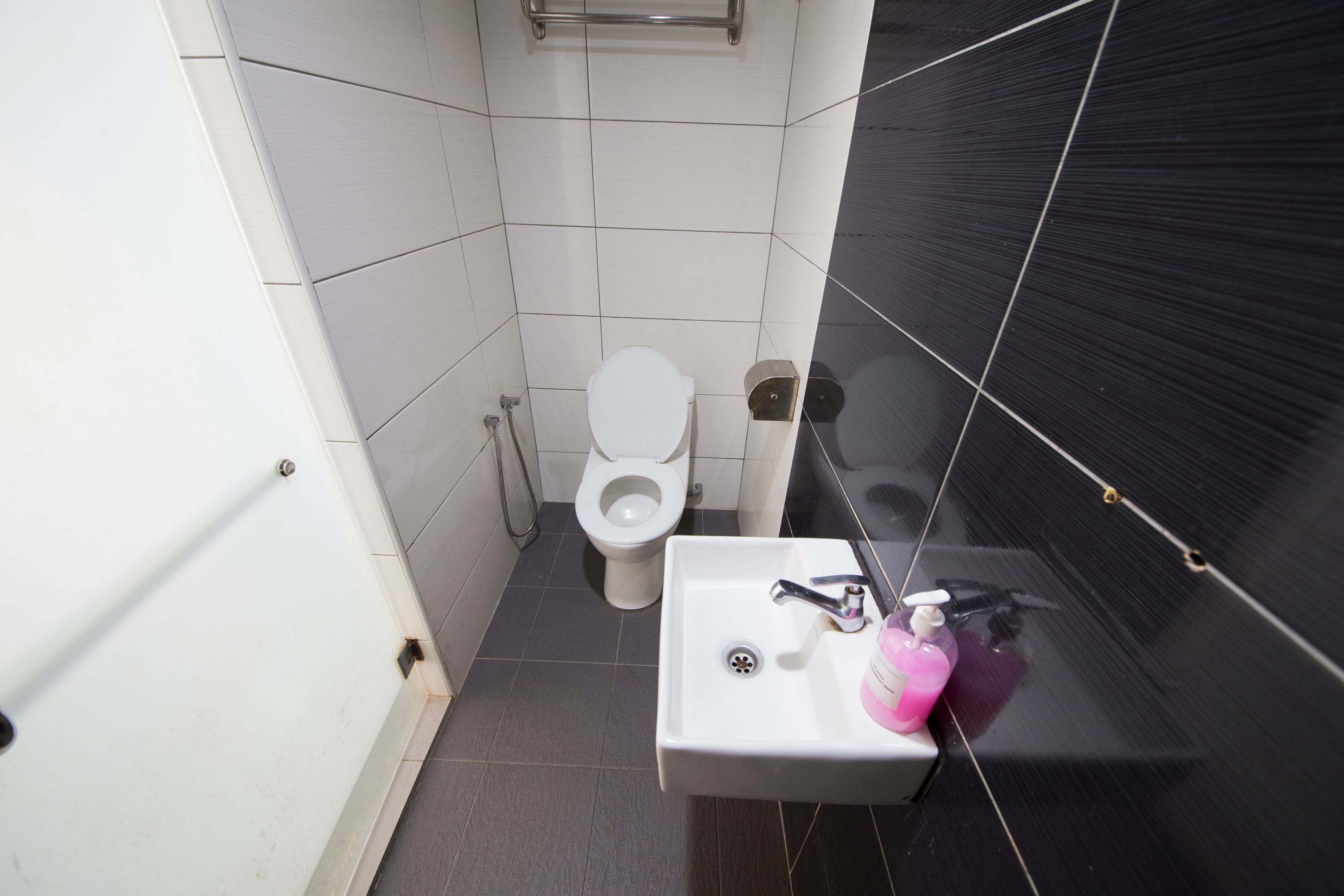 Et lille badeværelse med toilet, vask med sæbedispenser og spejl.
