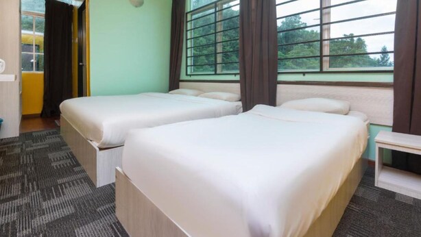 A hotel room with two beds, a small table, and a window with curtains. - Madani Hotel Cameron Highland (Tanah Rata)