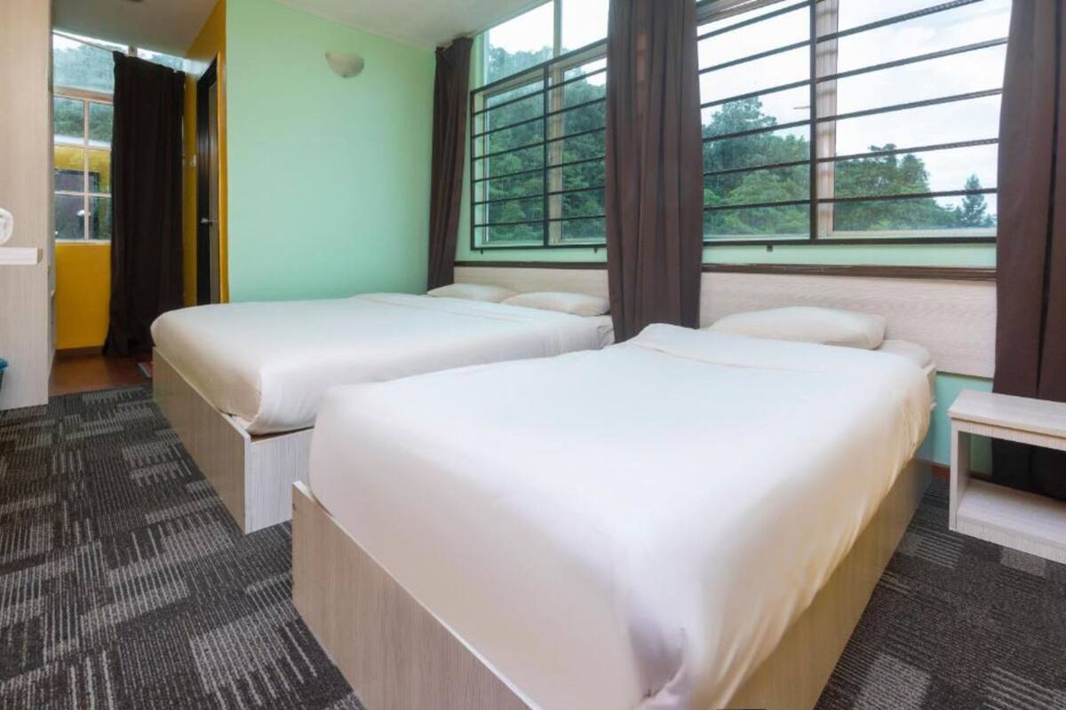 A hotel room with two beds, a small table, and a window with curtains.