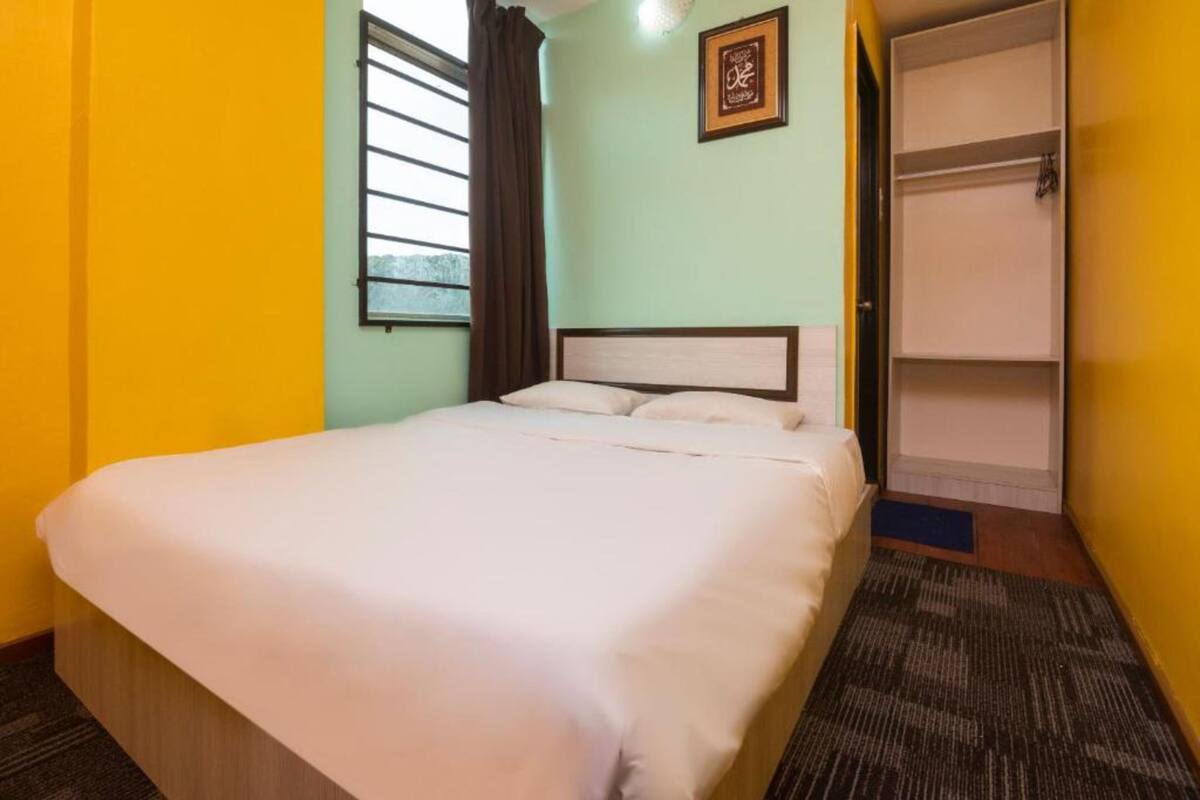 A hotel room with a bed, a window with blinds, a wall-mounted shelf, and a door leading to a closet.