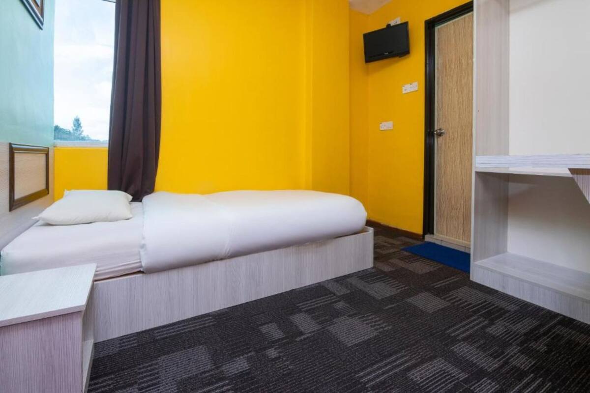 A hotel room with two beds, a television on the wall, and a window with curtains.
